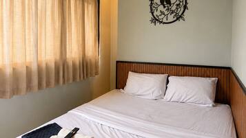Quarto de hotel com cama, ar-condicionado fixado na parede, janela com cortinas e um objeto decorativo na parede.