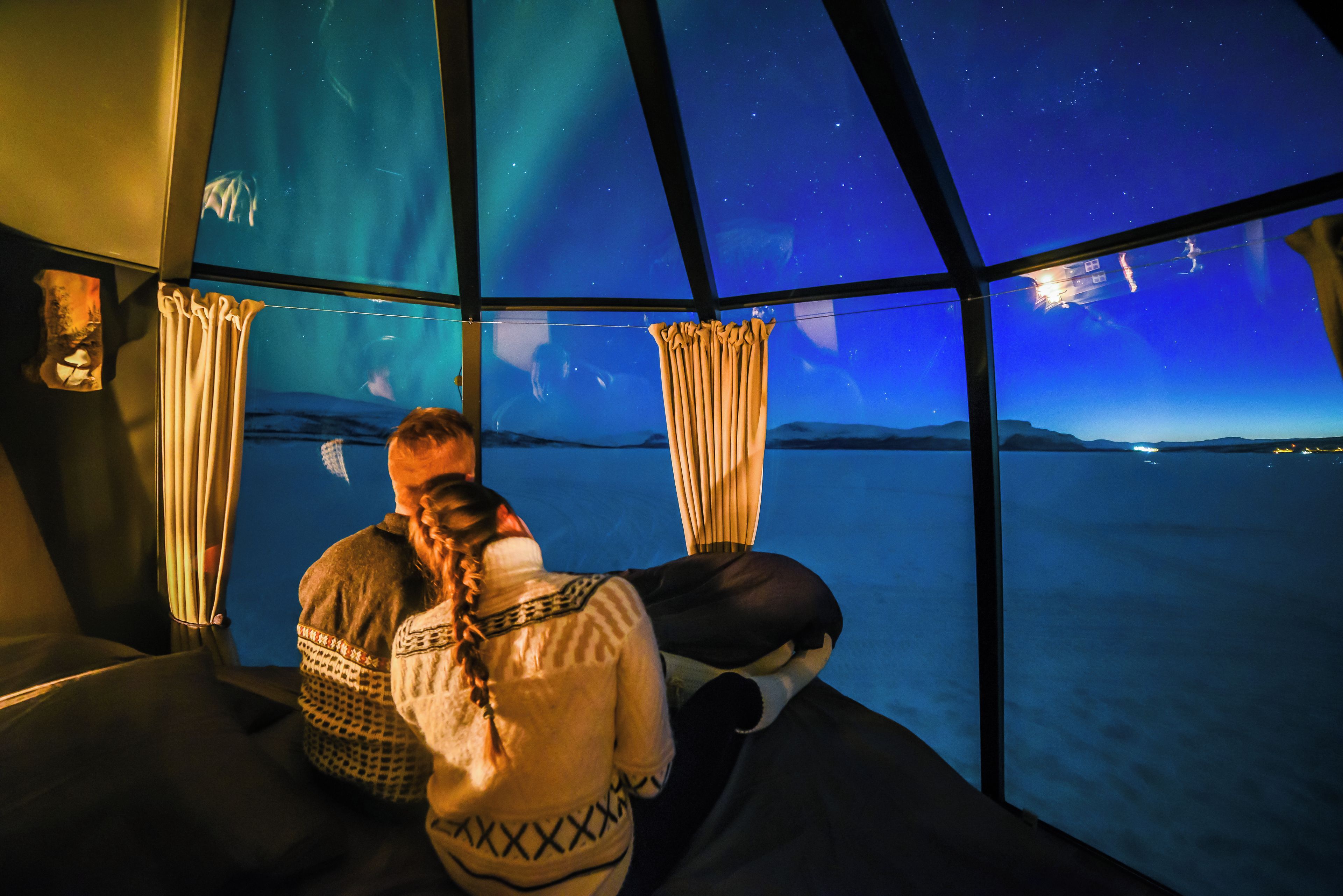 A room with a starry night view through a large window, a bed, and curtains.