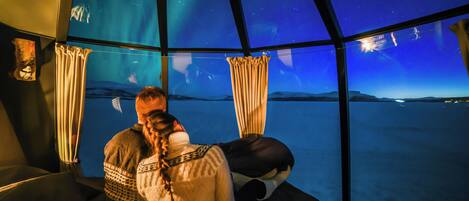 A room with a starry night view through a large window, a bed, and curtains.