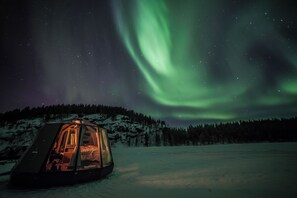 A snow-covered landscape with a tent-like structure and a view of the northern lights.