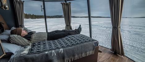 A room with a bed, a window, and a view of a snowy landscape.