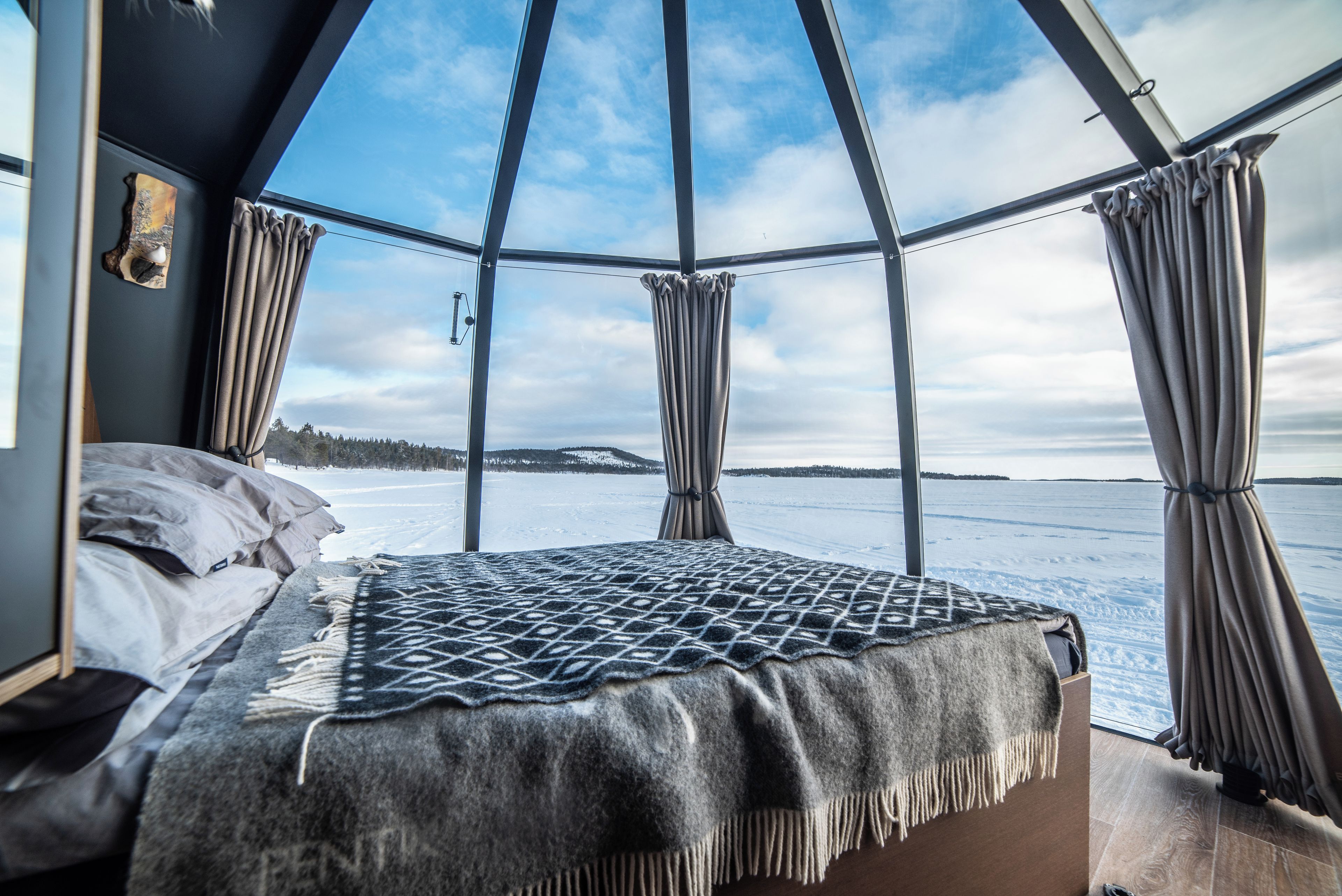 A room with a bed, a view of a snowy landscape through large windows, and curtains.