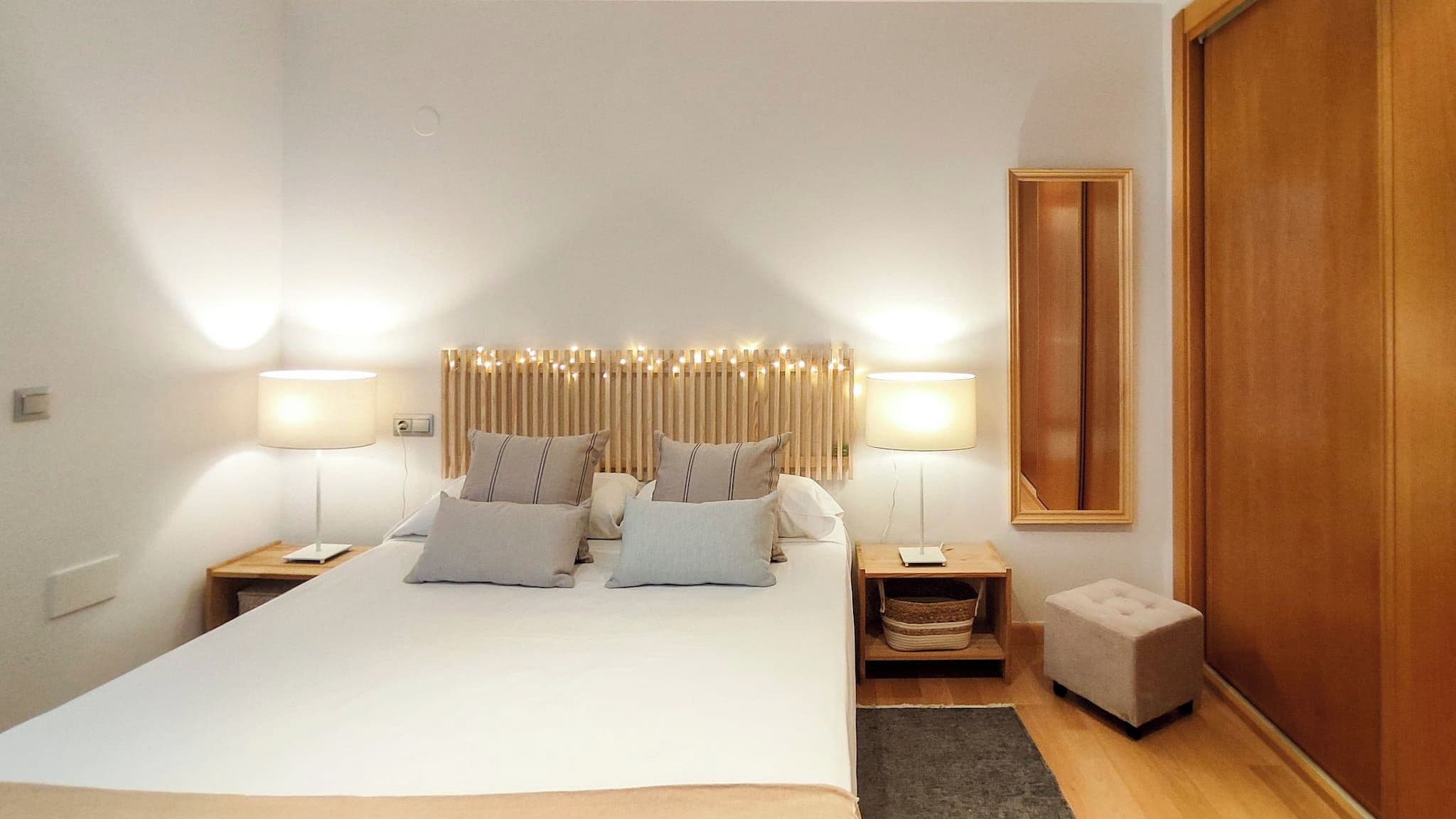 Une chambre à coucher bien rangée, avec un grand lit, deux tables de chevet, un petit banc et une armoire en bois.