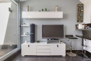 A modern kitchen with a flat-screen TV, white cabinetry, and a bar area with stools. - Cap Agde Waterfront (Agde)