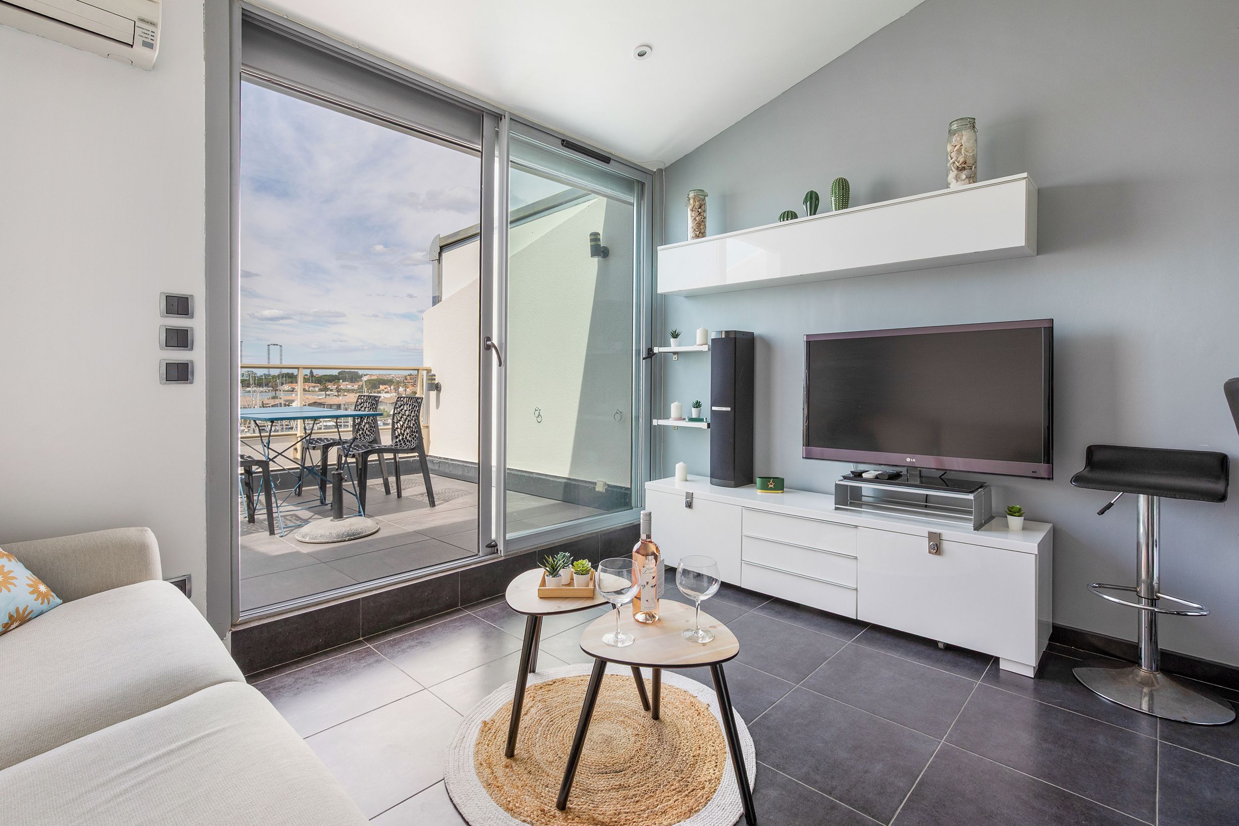 A modern living room with a large TV, a sofa, a dining area, and a balcony with a view.