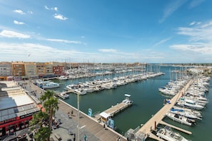 A marina with numerous boats docked, a waterfront promenade, and buildings in the background. - Cap Agde Waterfront (Agde)