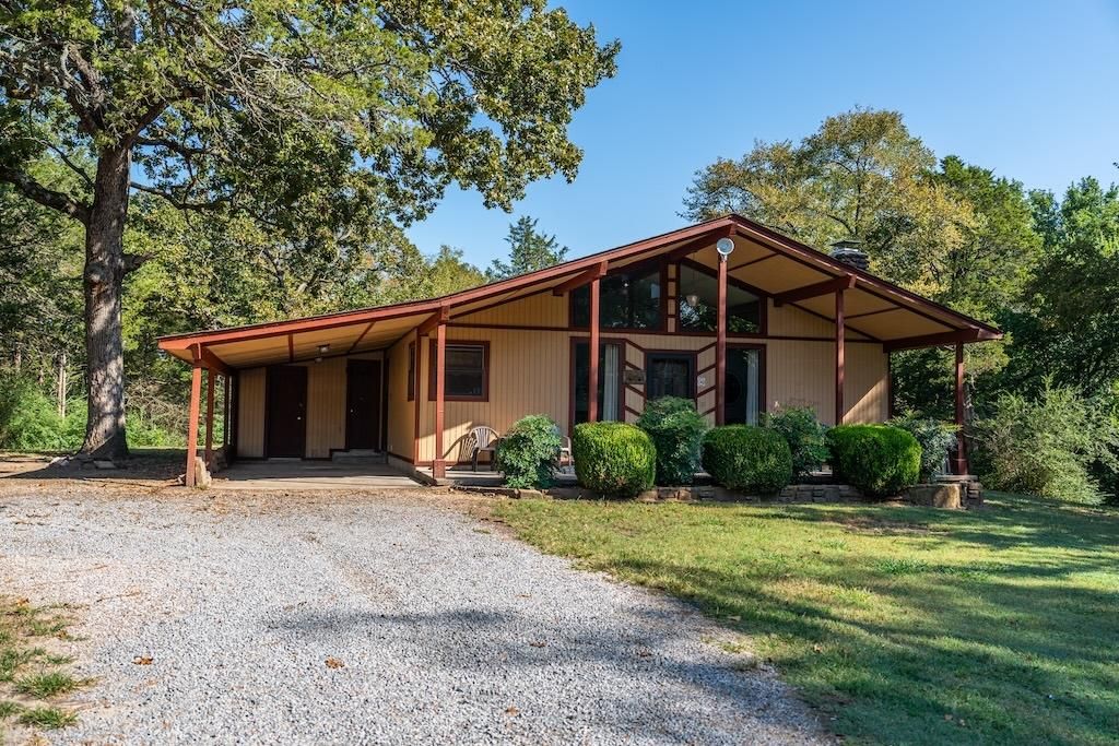 A two-story wooden house with a covered porch, a gravel driveway, and a well-maintained lawn.