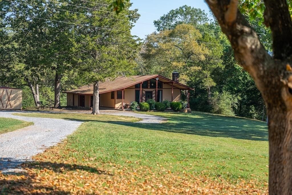 Een gelijkvloers huis met een veranda, omringd door een verzorgd gazon en bomen.