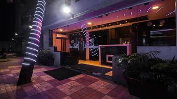 A hotel entrance with a glass facade, a reception desk, and a neon light installation.