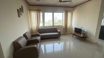 A living room with a sofa set, a television, and a window with curtains.