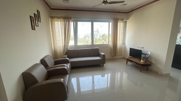A living room with a sofa set, a television, and a window with curtains.