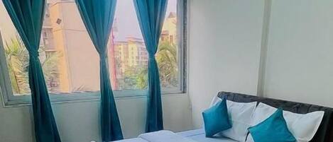 A neatly made bed with a white and teal bedspread, a ceiling fan, and an air conditioning unit above a window with teal curtains.