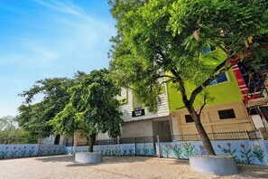 Un hotel con fachada verde, un cartel y un patio empedrado con macetas.