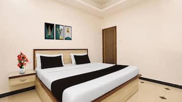 Ein Hotelzimmer mit einem Bett, einem Nachttisch, einer Blumenvase und drei gerahmten Bildern an der Wand.