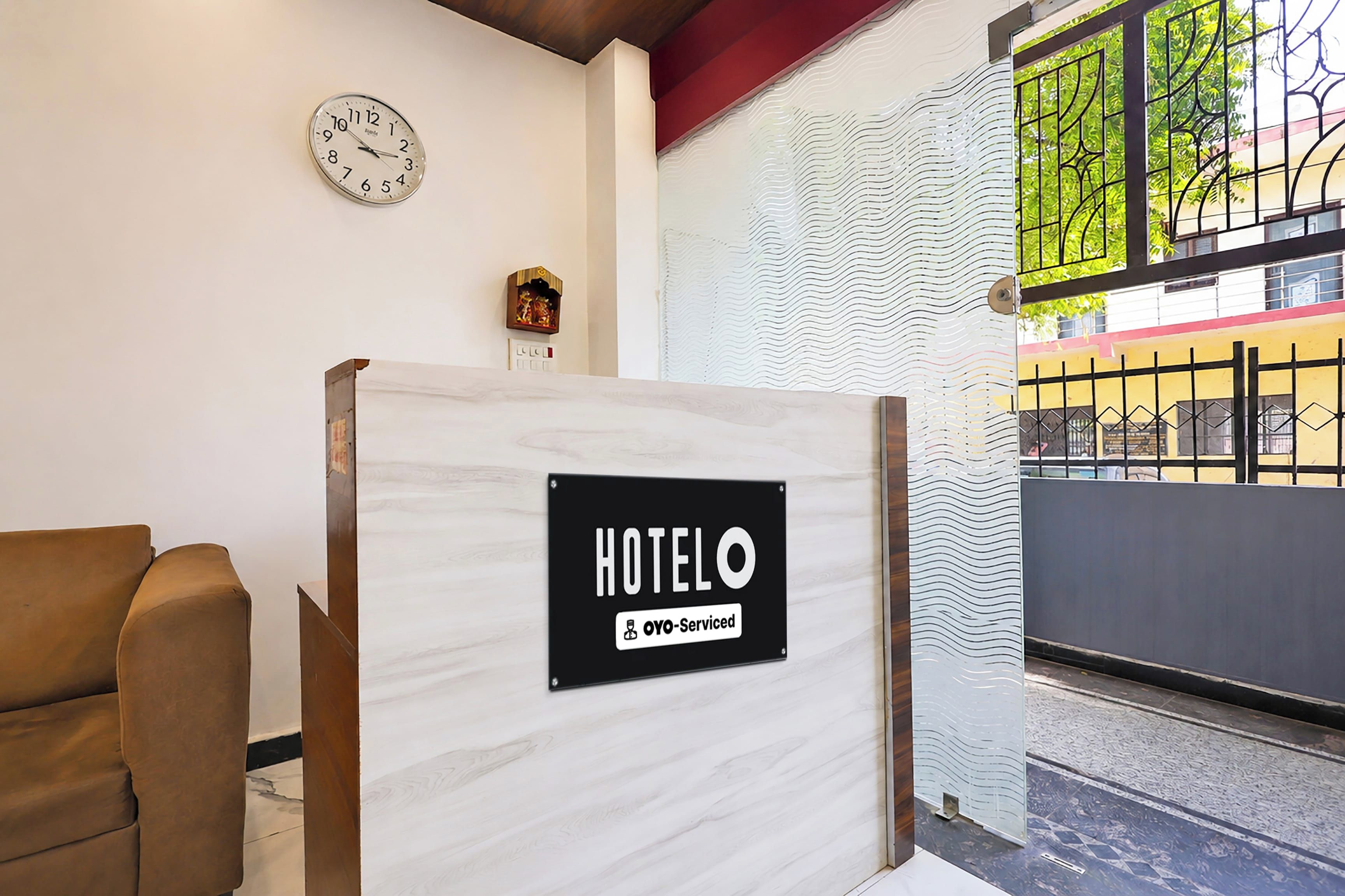 Zona de recepción de hotel con un mostrador de madera, un reloj en la pared y un cartel que indica que el hotel es 'YOYO-Serviced'.