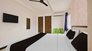 Habitación de hotel con cama, ventilador de techo, televisor de pantalla plana, dos puertas, unidad de aire acondicionado y dos sillas verdes.