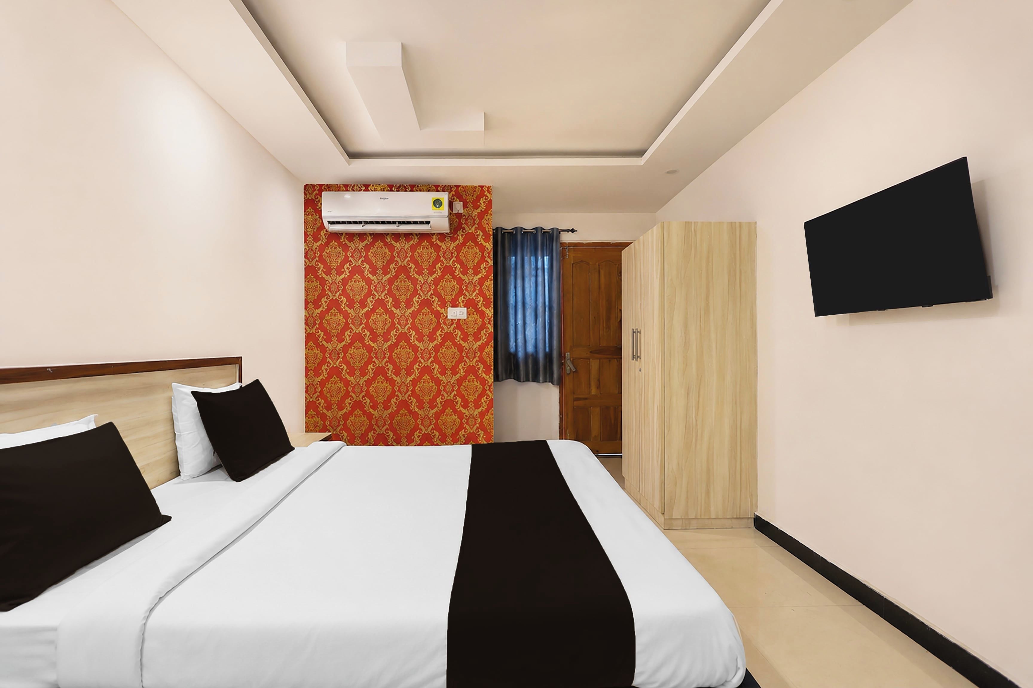 A hotel room with a bed, an air conditioning unit, a wardrobe, and a television mounted on the wall.