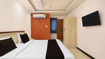 A hotel room with a bed, an air conditioning unit, a wardrobe, and a television mounted on the wall.