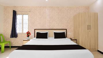 Habitación de hotel con cama, mesita de noche, una silla verde, armario y ventana con cortinas.