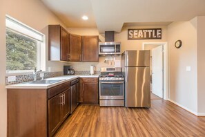A modern kitchen with wooden cabinets, stainless steel appliances, a dishwasher, and a view of the outdoors. - Perfect 2-bedroom Guest Suite with AC in welcoming Seattle (Seattle)