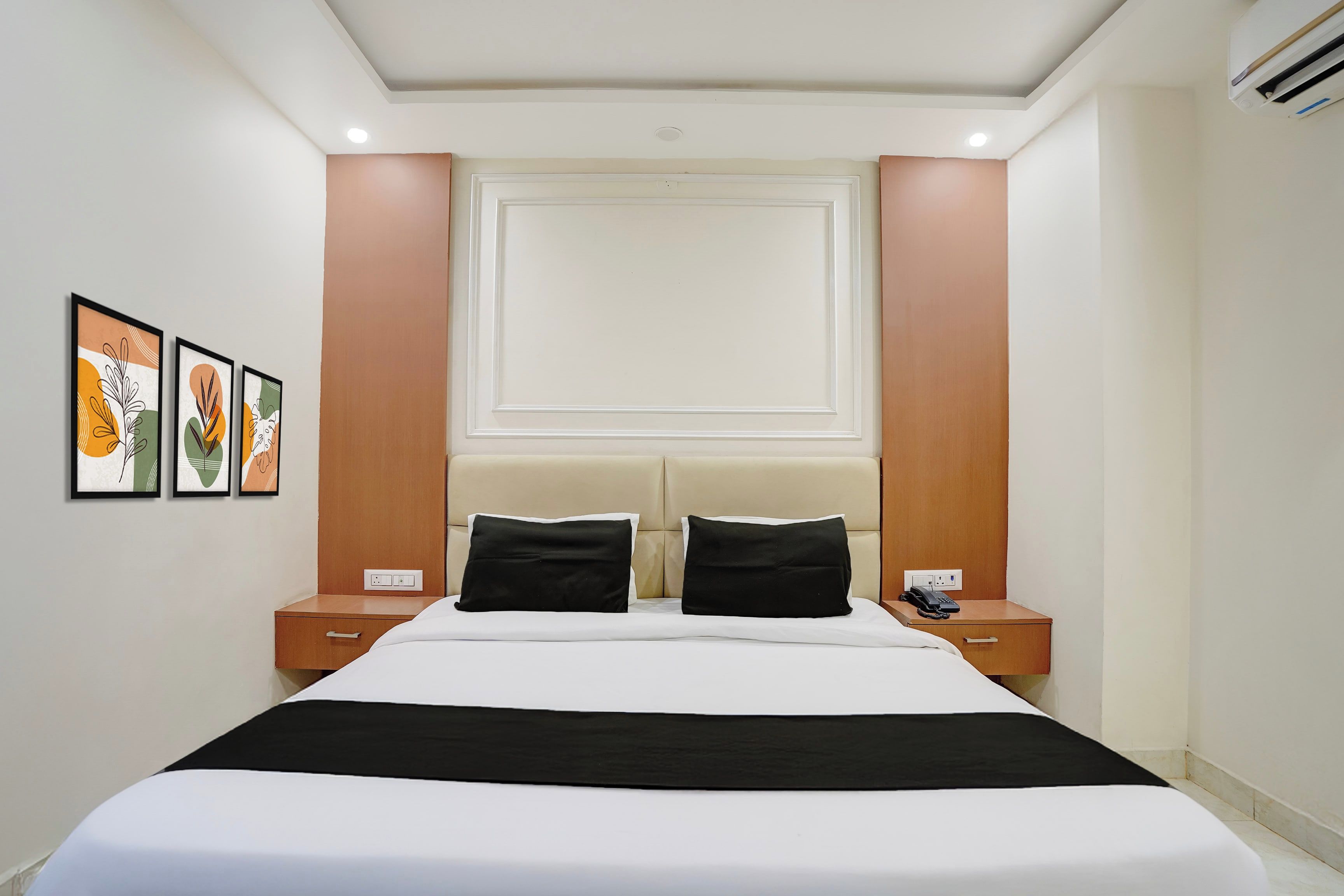 A hotel room with a bed, two bedside tables, a telephone, and framed artwork on the wall.