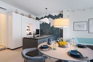 A modern kitchen with white cabinetry, a dining area with a round table set for two, and a blue sofa in the background. - Charming sea front apartment with terrace in Mazzarò, Taormina - DICasaInSicilia (Taormina)