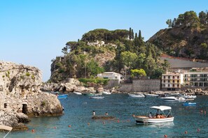 A coastal scene with rocky cliffs, a clear blue sky, and a marina with boats. - Charming sea front apartment with terrace in Mazzarò, Taormina - DICasaInSicilia (Taormina)