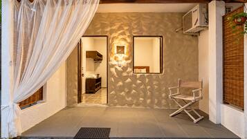 A room with a bed, a chair, a mirror, and a window with curtains.