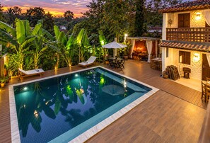A swimming pool with lounge chairs and umbrellas, surrounded by lush vegetation and a wooden deck.