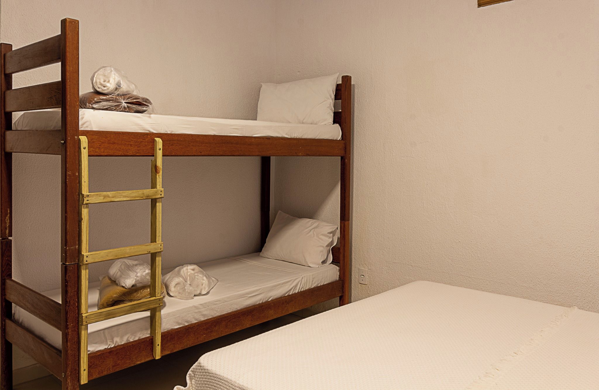 Uma cama box com beliche, escada, um colchão na parte inferior com travesseiro e um colchão no chão.
