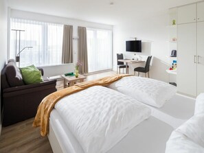 Ein Hotelzimmer mit Bett, Schreibtisch, Sessel, Sofa und Fernseher.