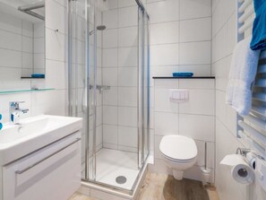Ein Badezimmer mit einer gläsernen Duschkabine, einem weißen Waschbecken, einer Toilette und einem Handtuchhalter.