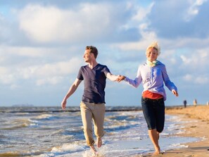 Zwei Personen halten Händchen und gehen am Strand entlang.