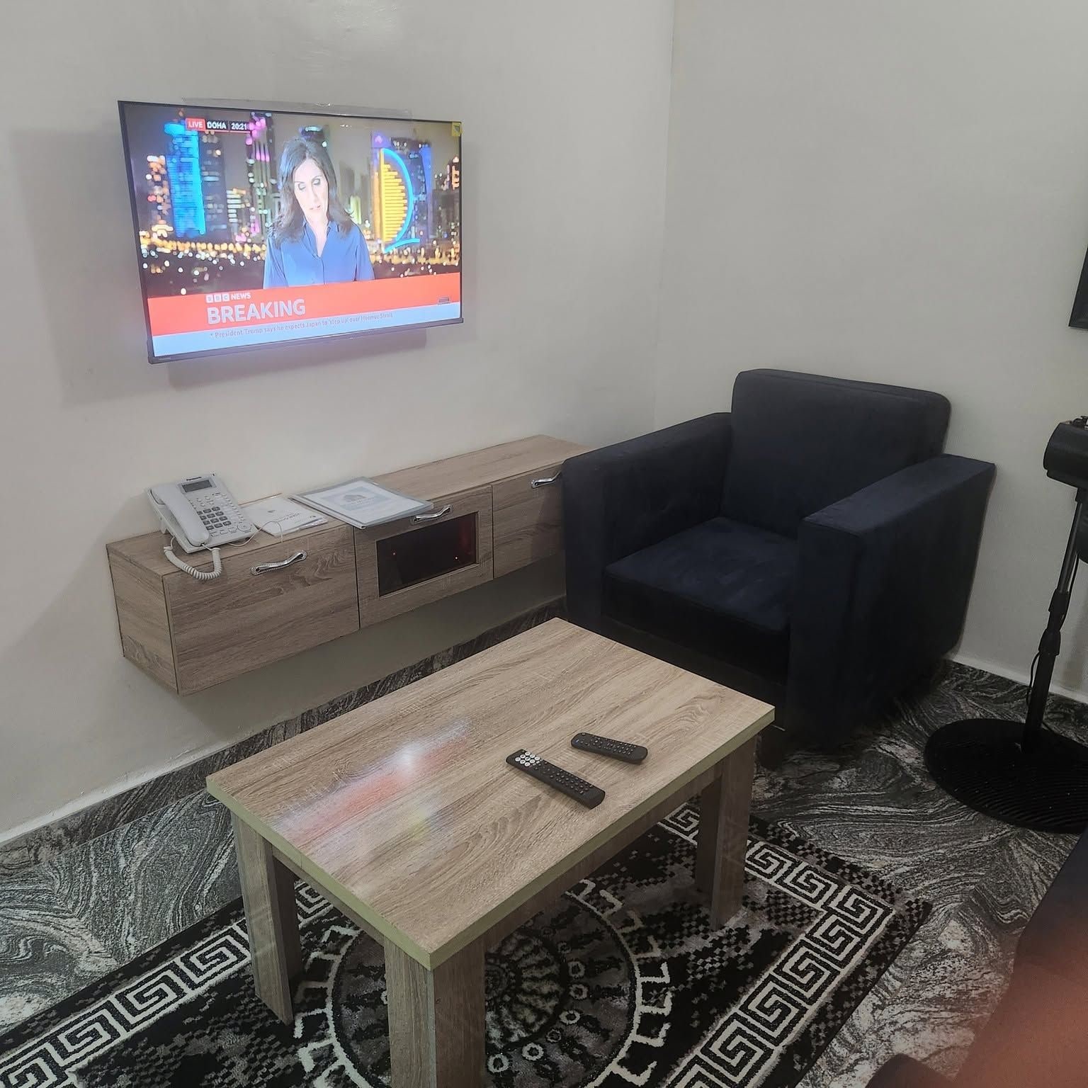 Un soggiorno con televisore che mostra un notiziario, un divano, un tavolino da caffè e un tappeto decorato.