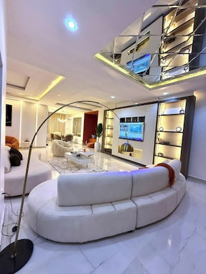 Ein modernes Wohnzimmer mit einer gebogenen weißen Couch, einem Flachbildfernseher und einer Glastreppe.