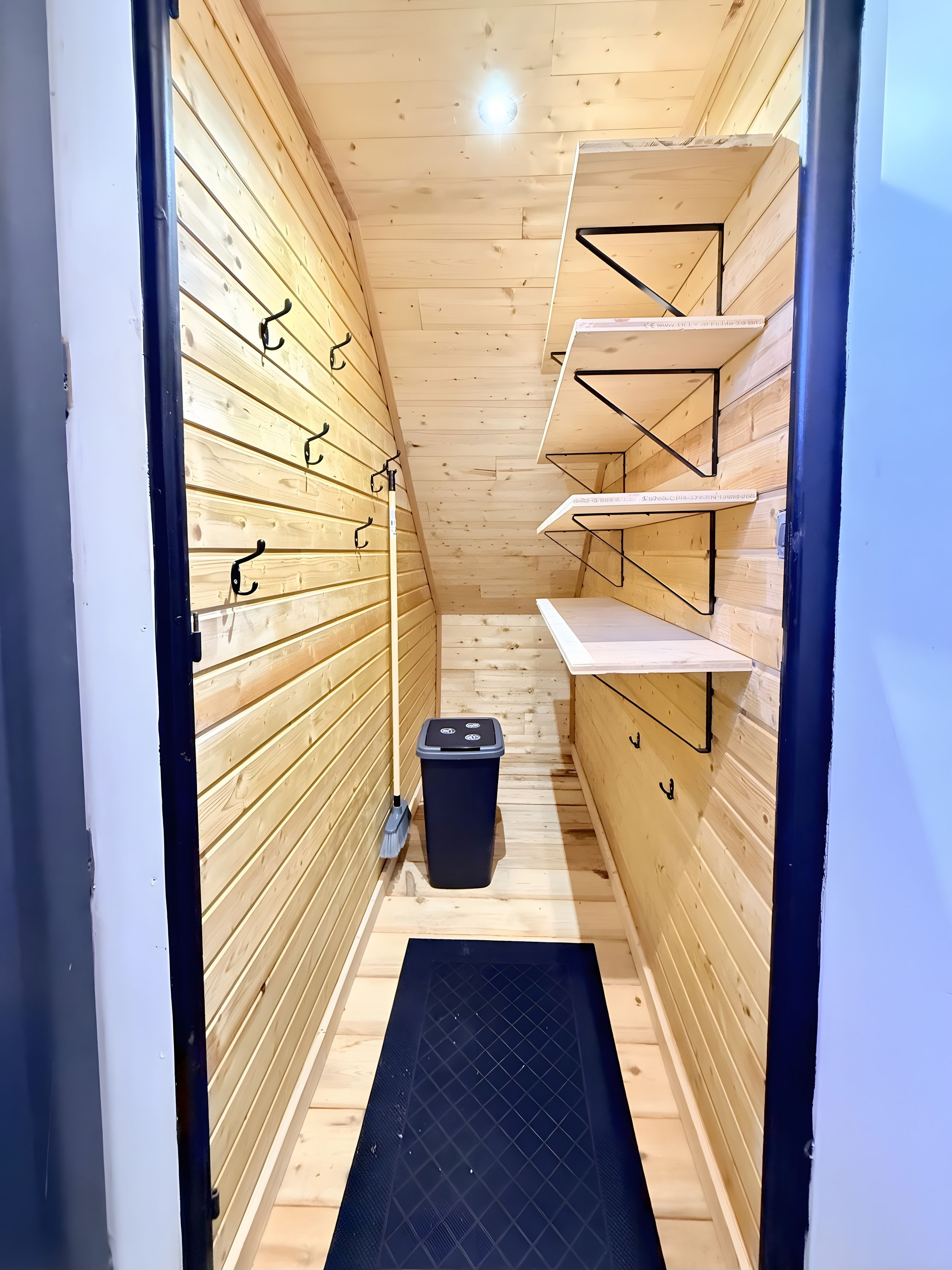 A narrow hallway with wooden walls, a black trash bin, and metal hooks on the walls.