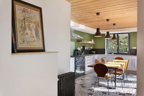 A modern kitchen with a dining area, featuring a stove, oven, and hanging pendant lights.
