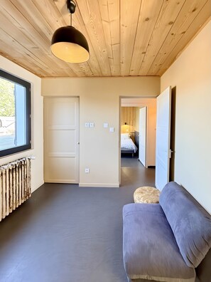 Una habitación con techo de madera, un sofá, un radiador y una puerta que da a otra estancia.