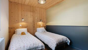 Une chambre avec deux lits simples, des murs recouverts de panneaux de bois, un luminaire au plafond et un radiateur.