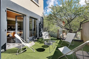 A patio with artificial grass, white lounge chairs, and a glass door leading to an interior space.