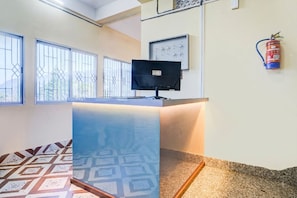 Un mostrador de recepción con un monitor de computadora, un extintor y un panel de control en la pared.