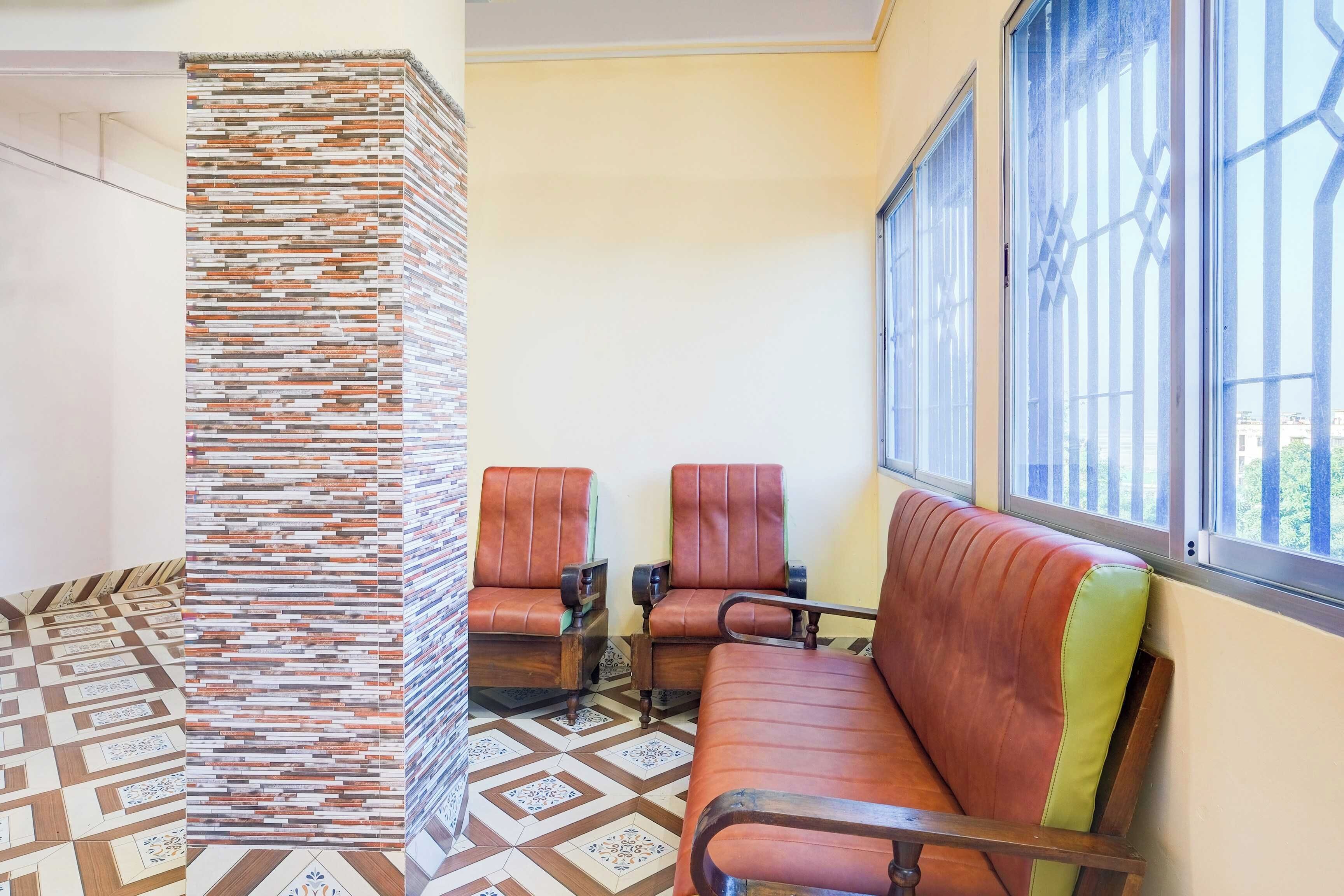 Un área de espera con un muro estampado, dos sillones de cuero, un banco y una ventana con vistas.