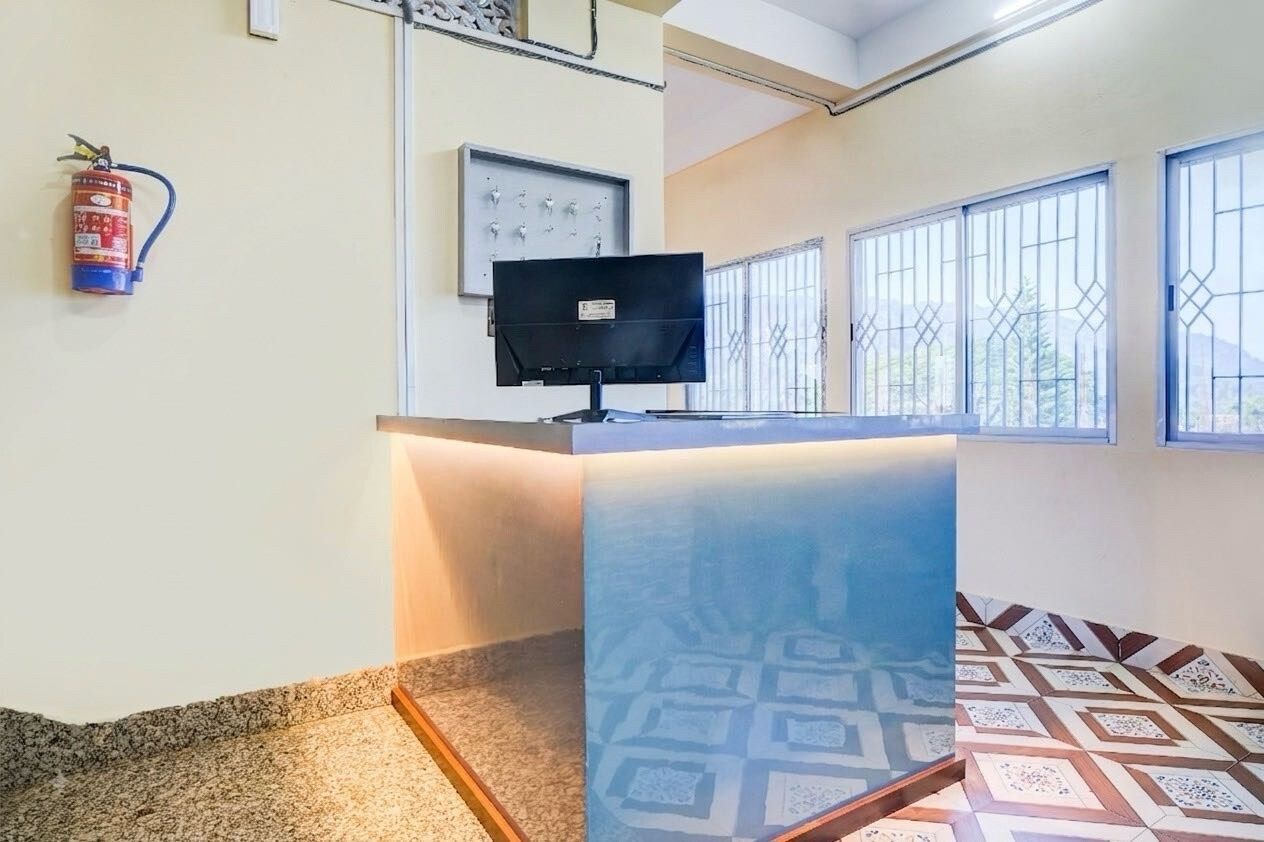 A reception area with a counter, a fire extinguisher, a wall-mounted television, and patterned floor tiles.