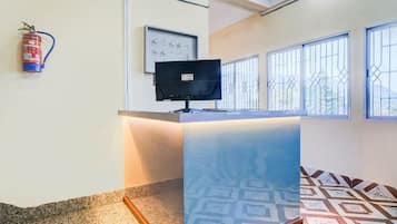 A reception area with a counter, a fire extinguisher, a wall-mounted television, and patterned floor tiles.