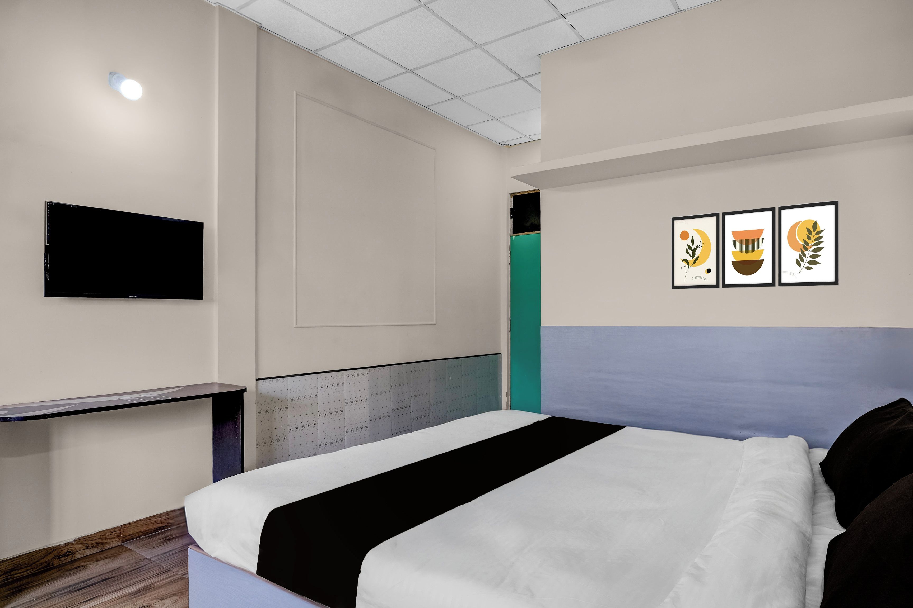 Habitación de hotel con cama, televisor de pantalla plana en la pared y tres obras de arte enmarcadas.