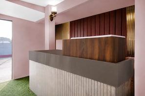 A reception desk with a wooden panel backdrop and a modern light fixture above it. - Collection O Jalukbari Bus Stand (Guwahati)