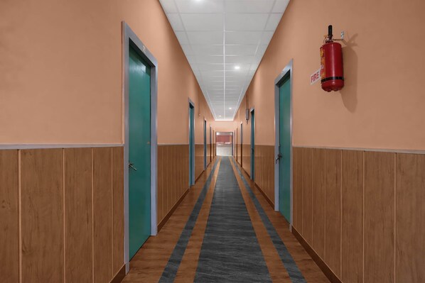 A hotel corridor with wooden paneling, teal doors, and a fire extinguisher mounted on the wall. - Collection O Jalukbari Bus Stand (Guwahati)