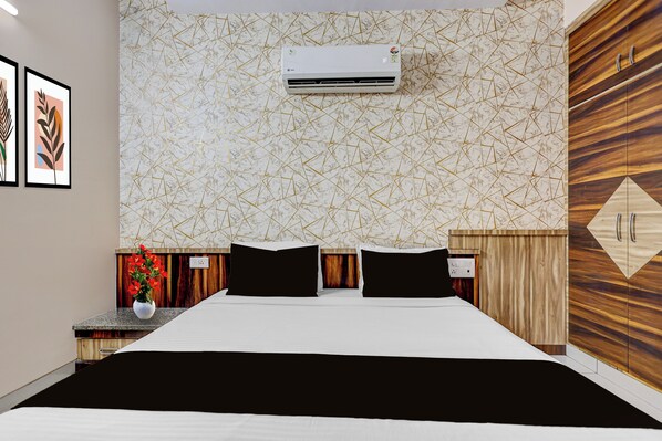 A hotel room with a bed, an air conditioning unit, a wooden wardrobe, and a wall with a geometric pattern.