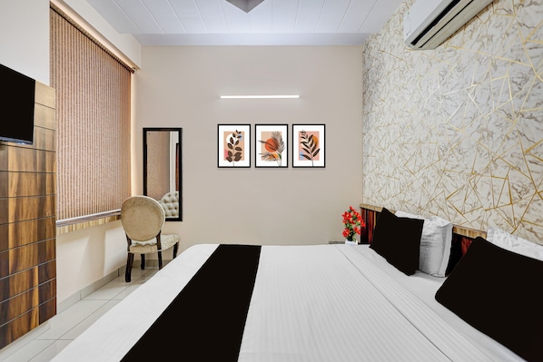 A hotel room with a bed, a chair, a wall-mounted air conditioner, and framed artwork.