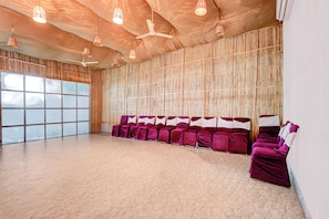Una habitación con pared de bambú, ventiladores de techo y una fila de sillas moradas.